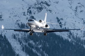 Business jet on final approach over snowy mountainous terrain, illustrating winter operations and the challenges of planning for wet and contaminated runway conditions.